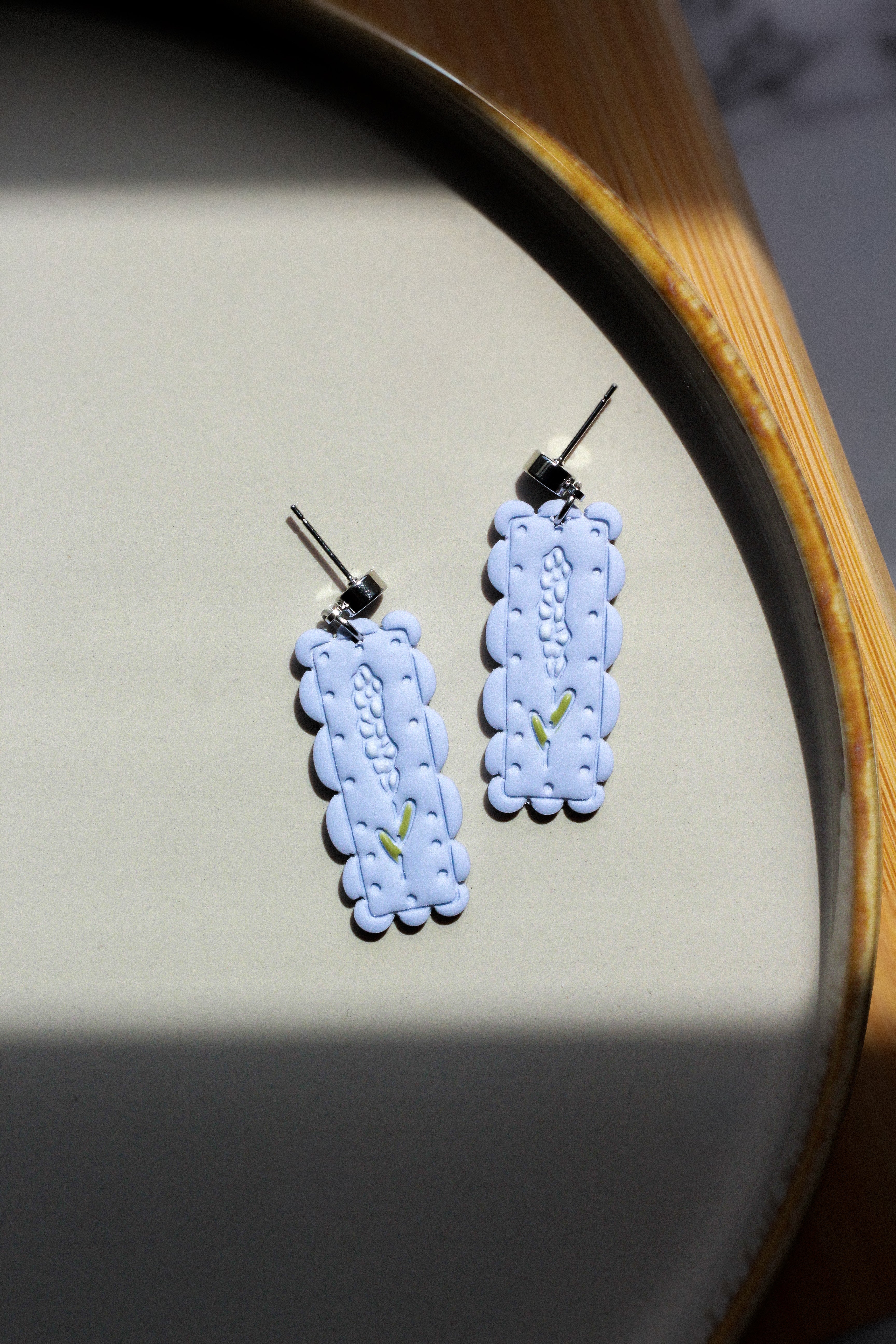 Light blue/purple embroidered earrings with white flowers on a round wooden surface