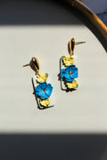 Floral earrings with blue and yellow flowers on a light gray surface.