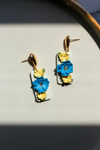 Floral earrings with blue and yellow flowers on a light gray surface.