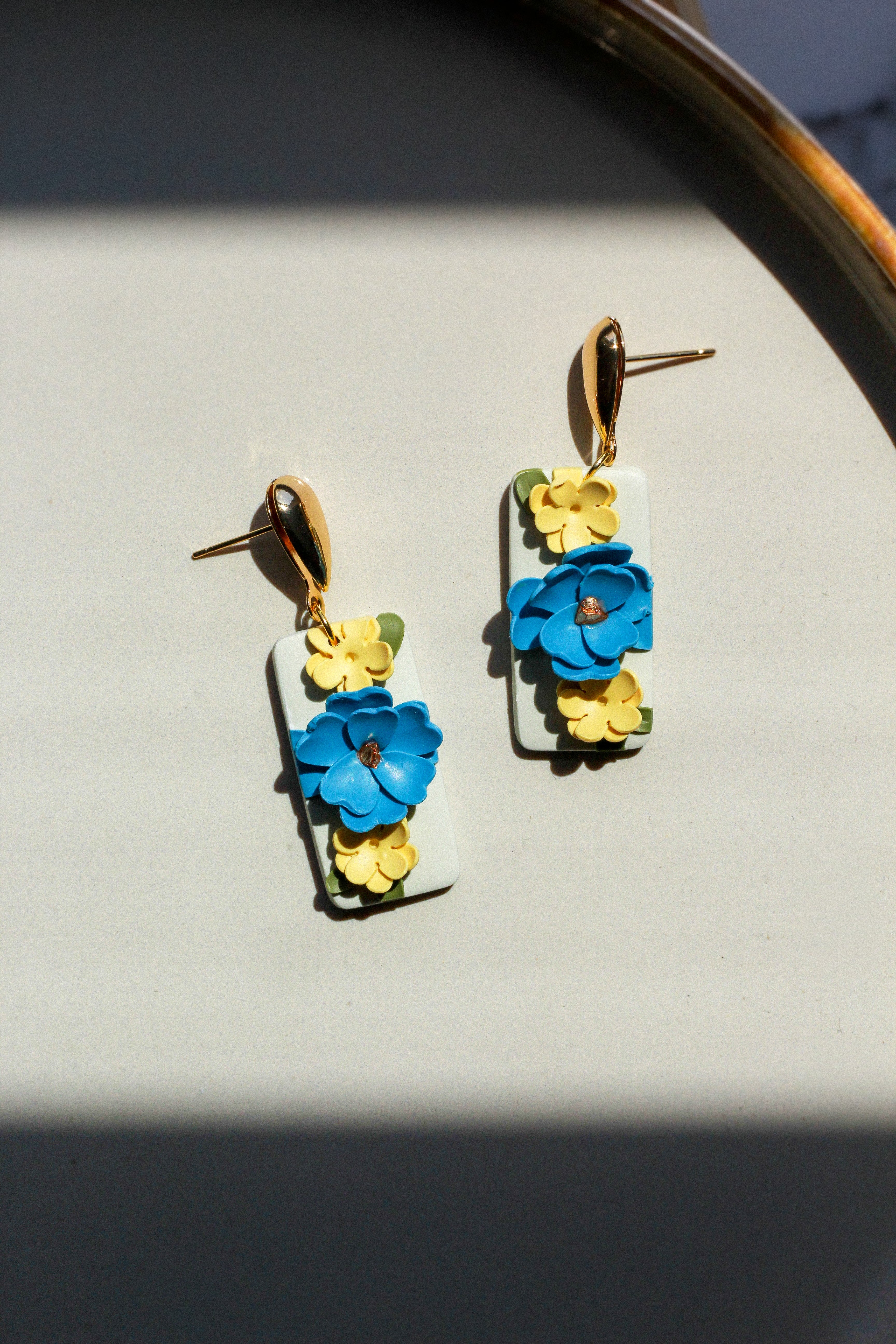 Floral earrings with blue and yellow flowers on a light gray surface.