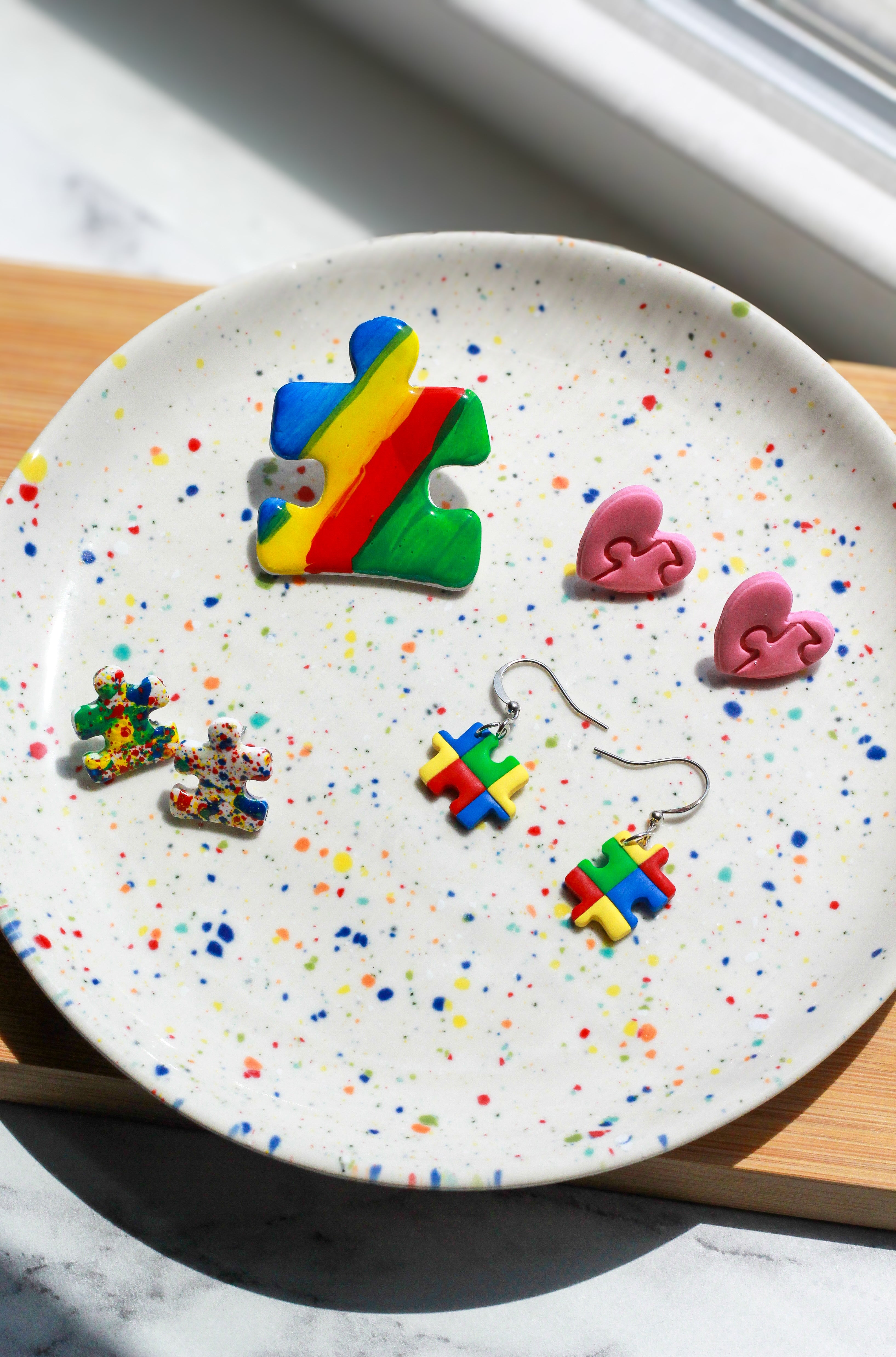 Colorful puzzle piece earrings on a speckled plate with a window in the background