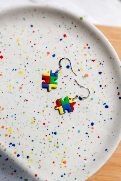 Colorful puzzle piece earrings on a speckled plate