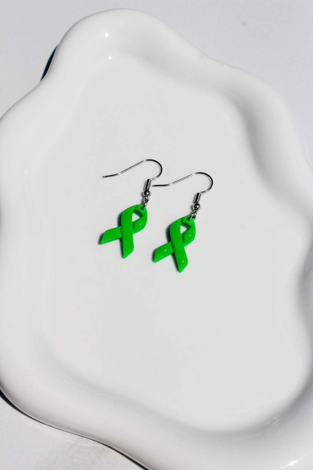 Green ribbon earrings on a white dish
