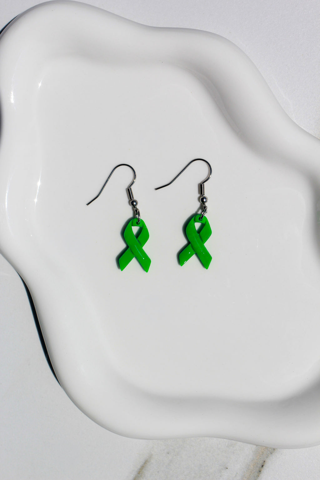 Green ribbon earrings on a white dish