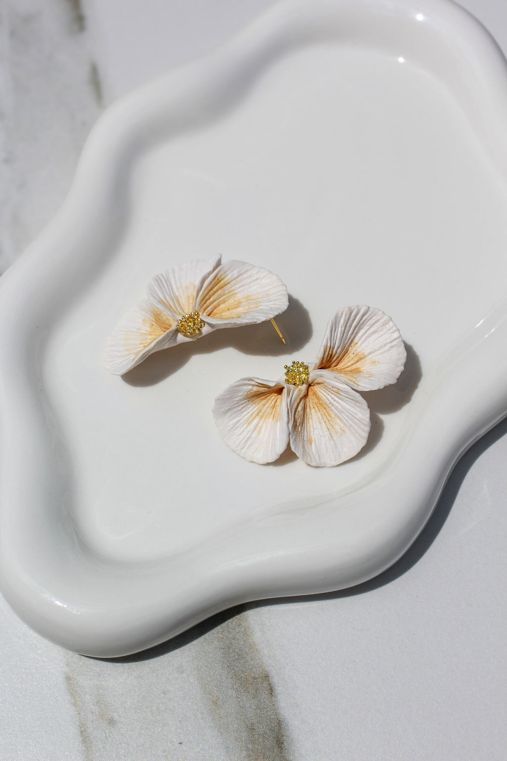 Floral earrings on a white ceramic dish with a marble background