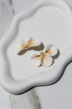 Floral earrings on a white ceramic dish with a marble background