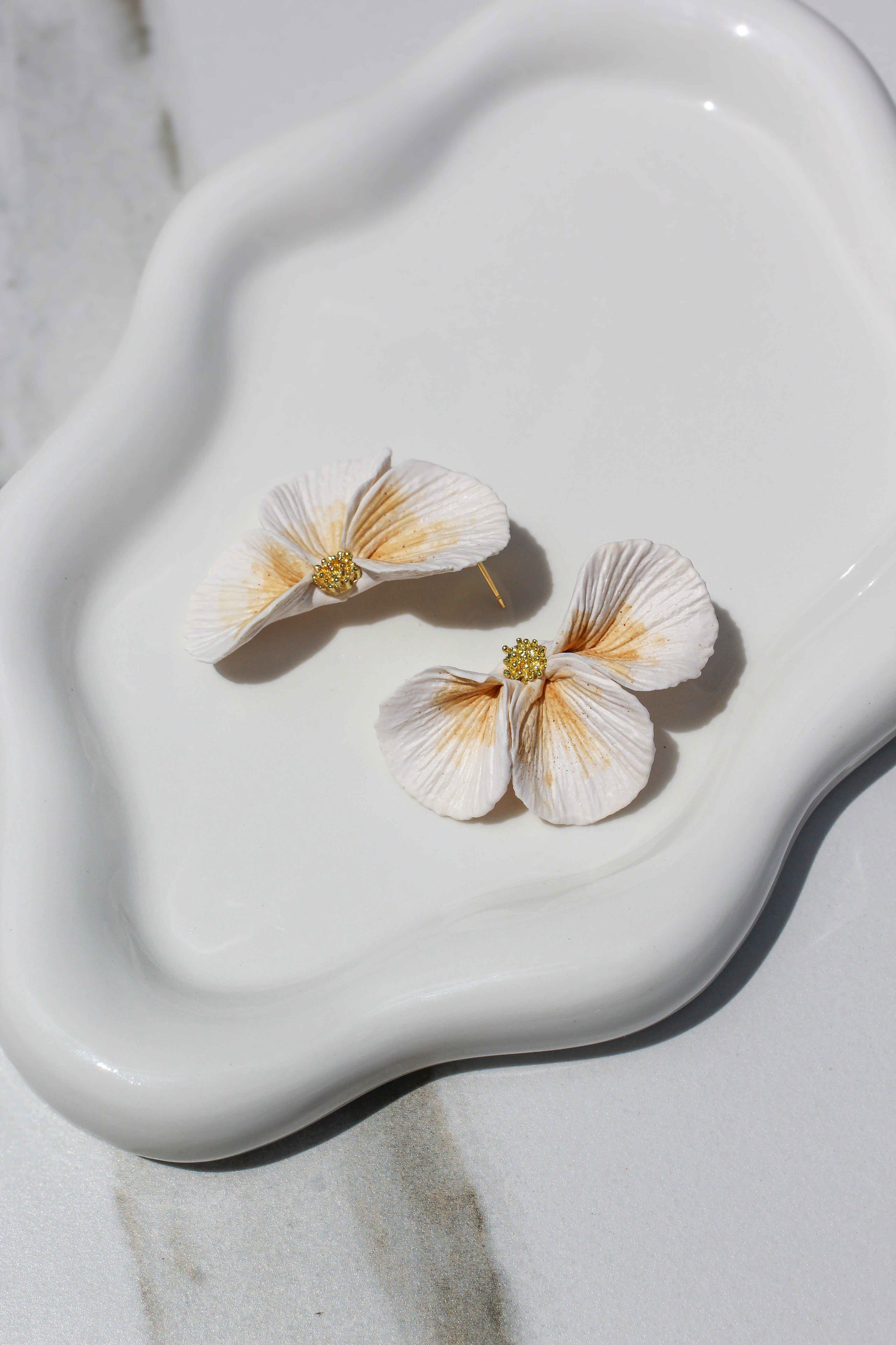 Floral earrings on a white ceramic dish with a marble background