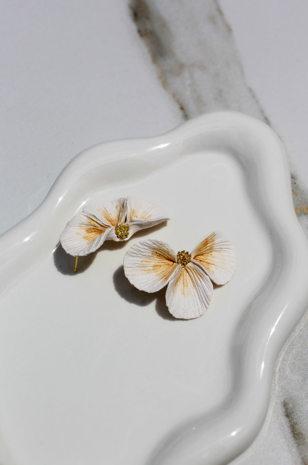Flower-shaped earrings on a white ceramic dish with a marble background