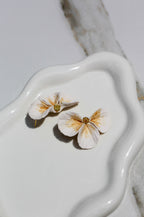 Flower-shaped earrings on a white ceramic dish with a marble background