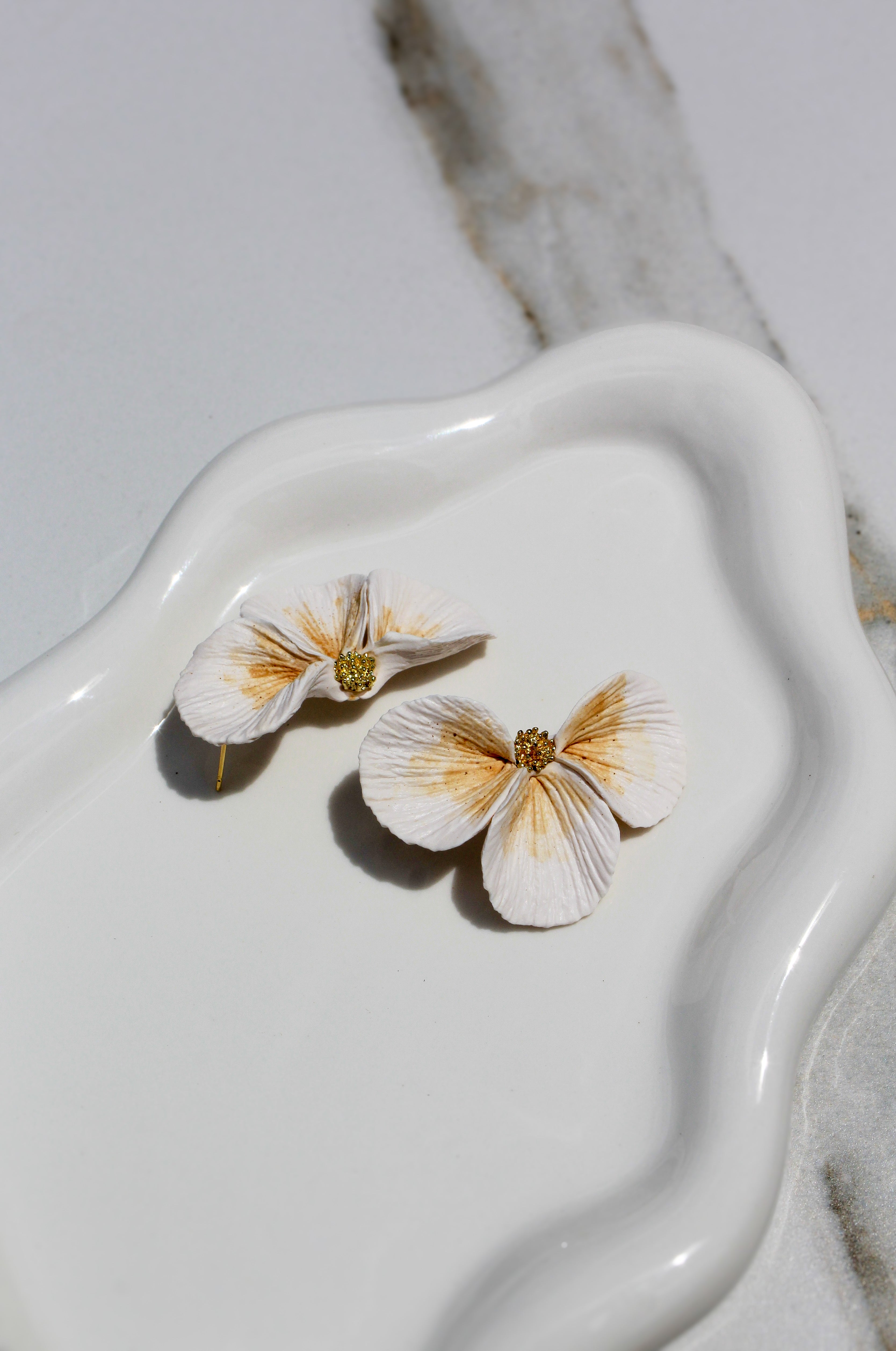 Flower-shaped earrings on a white ceramic dish with a marble background