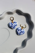 Pair of blue and white patterned earrings on a decorative white dish.