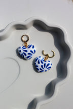 Pair of blue and white patterned earrings on a decorative white dish.