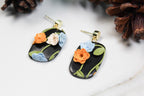 Floral earrings on a white surface with pine cones in the background