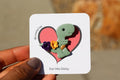 Card with a dinosaur pin with flowers and  held by a hand.