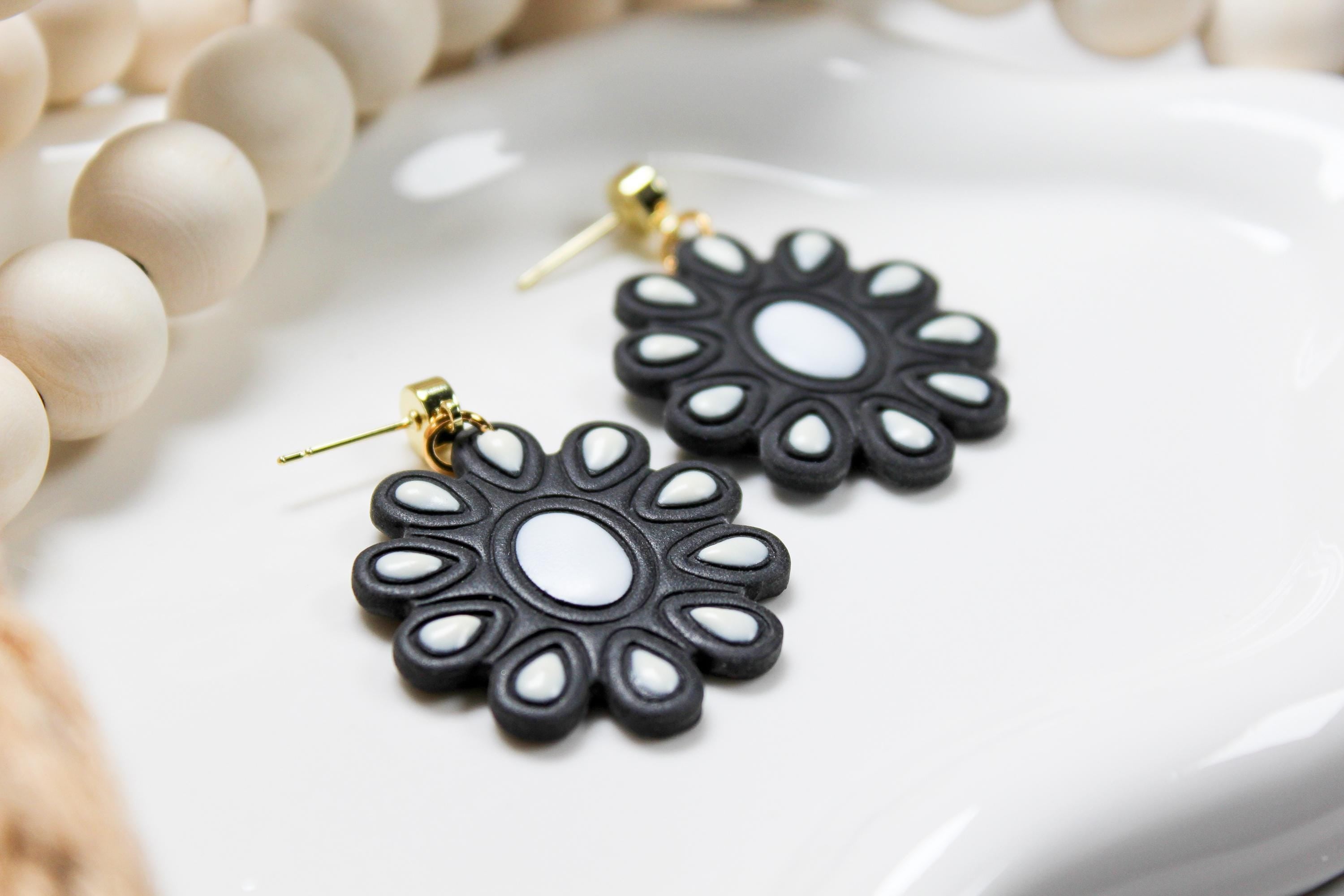 Black and white flower-shaped earrings on a white surface with beige beads in the background.