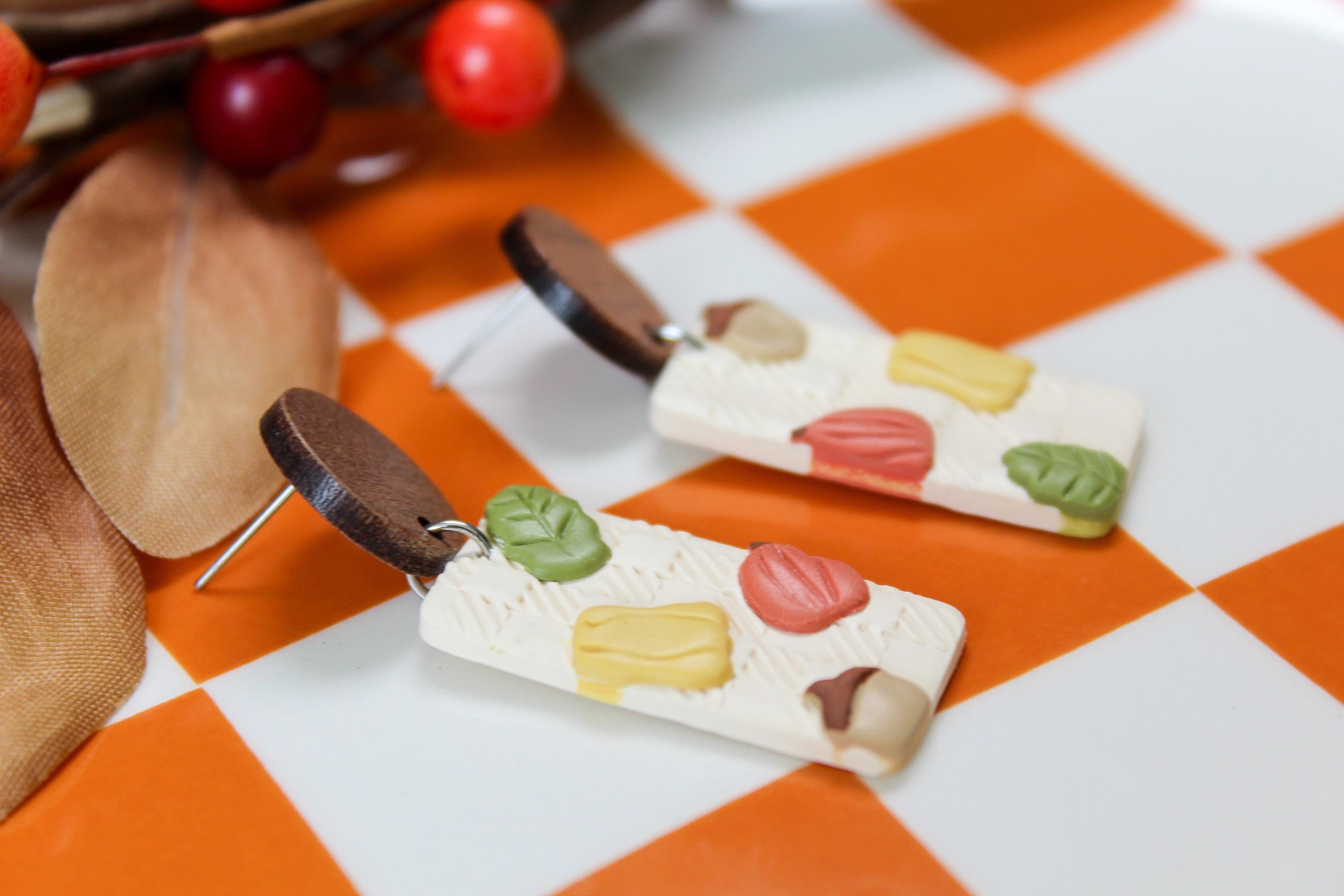 Wooden earrings with colorful autumn designs on a checkered orange and white background.