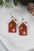 Christmas-themed earrings resembling gingerbread houses on a white surface.