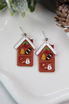 Christmas-themed earrings resembling gingerbread houses on a white surface.