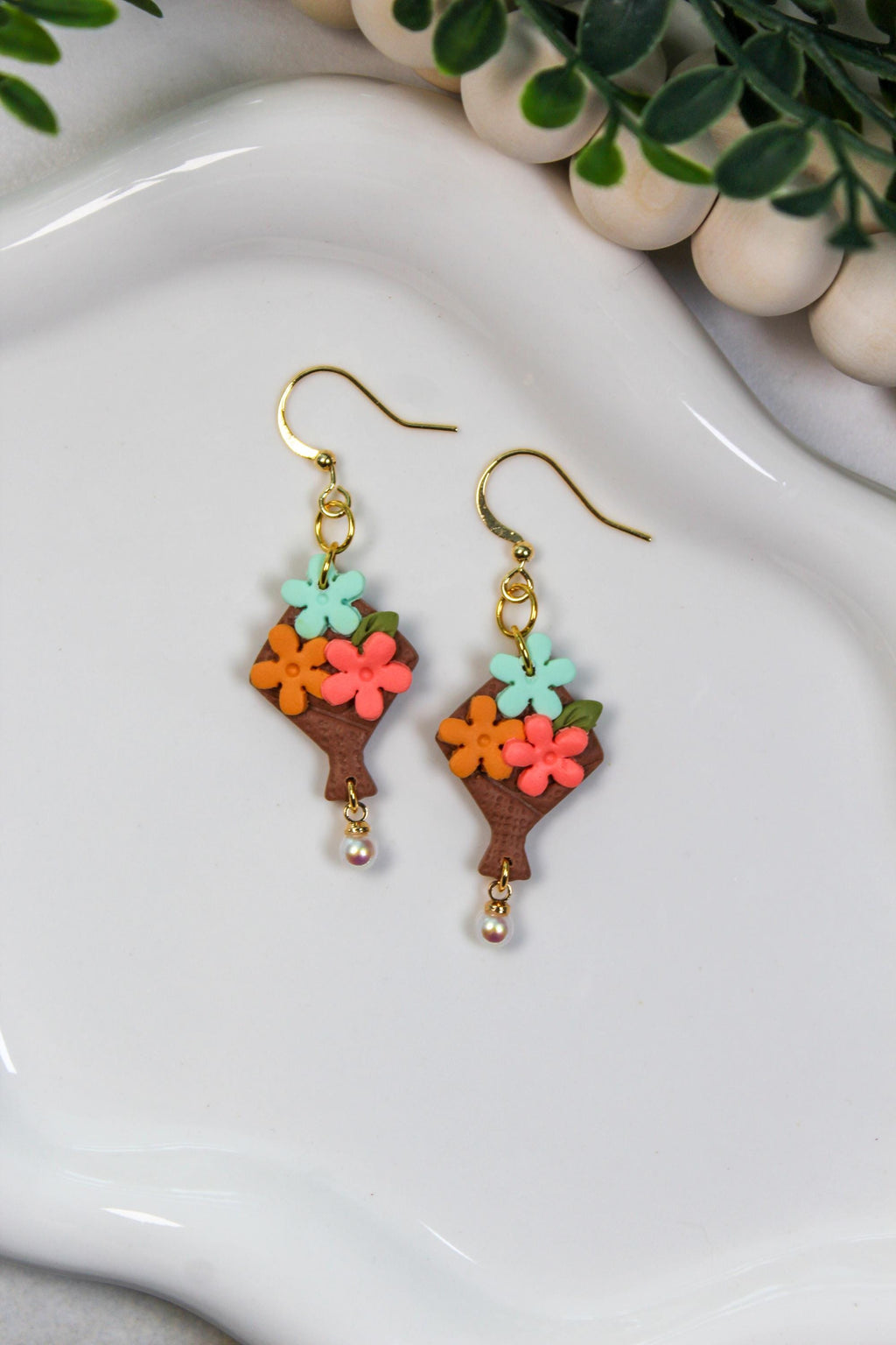 Colorful flower-shaped bouquet earrings on a white dish with a plant in the background