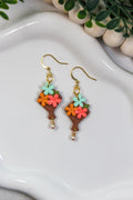 Colorful flower-shaped bouquet earrings on a white dish with a plant in the background