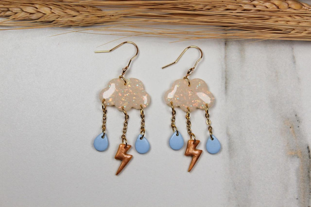Pair of cloud-shaped earrings with lightning bolt and droplet charms on a light background.