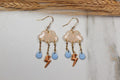 Pair of cloud-shaped earrings with lightning bolt and droplet charms on a light background.
