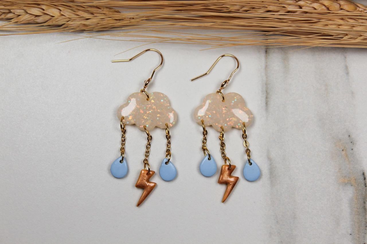 Pair of cloud-shaped earrings with lightning bolt and droplet charms on a light background.