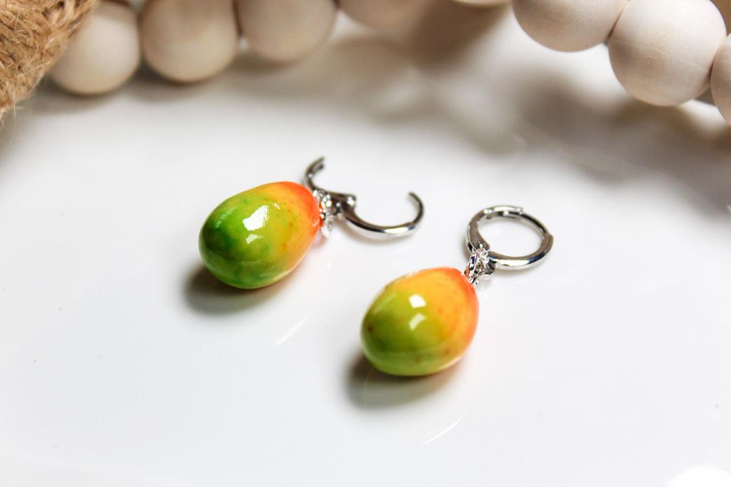 Pair of colorful mango-shaped earrings on a white surface with a blurred background.
