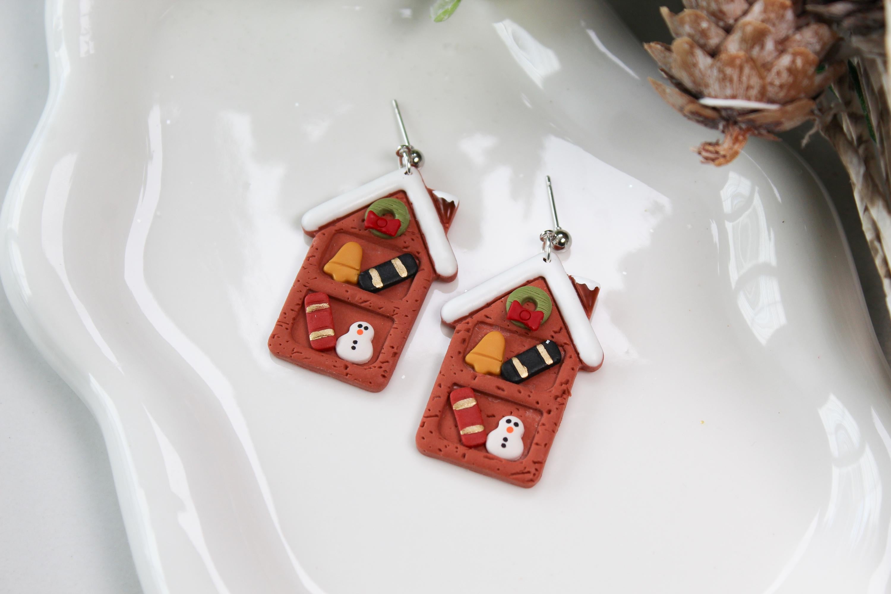 Christmas-themed gingerbread house earrings on a white dish with decorative elements.