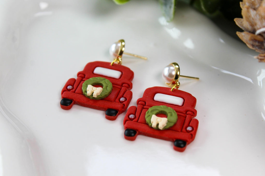 Red truck-shaped earrings with green wreaths on a white surface