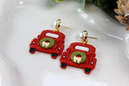 Red truck-shaped earrings with green wreaths on a white surface
