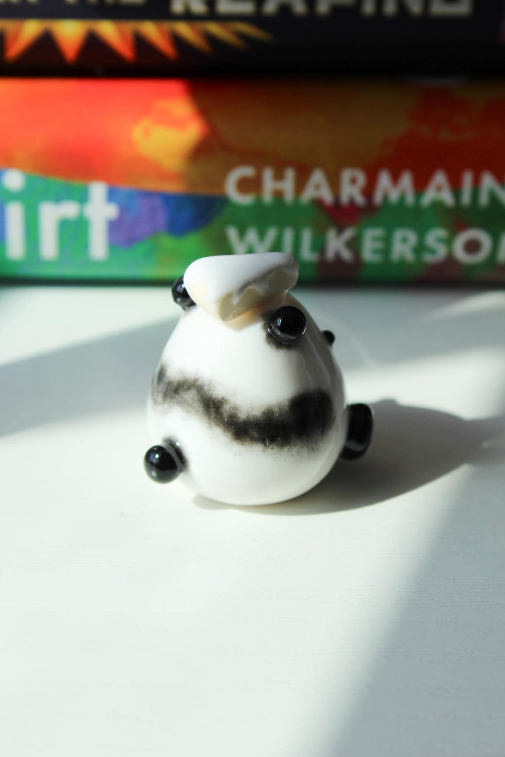 Small white figurine of a Panda with black accents and a piece of cake on a white surface, with a book titled 'Good Dirt' by Charmaine Wilkerson in the background.