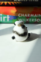 Small white figurine of a Panda with black accents and a piece of cake on a white surface, with a book titled 'Good Dirt' by Charmaine Wilkerson in the background.