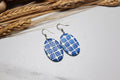 Blue patterned earrings on a light surface with dried wheat in the background