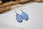 Blue patterned earrings on a light surface with dried wheat in the background