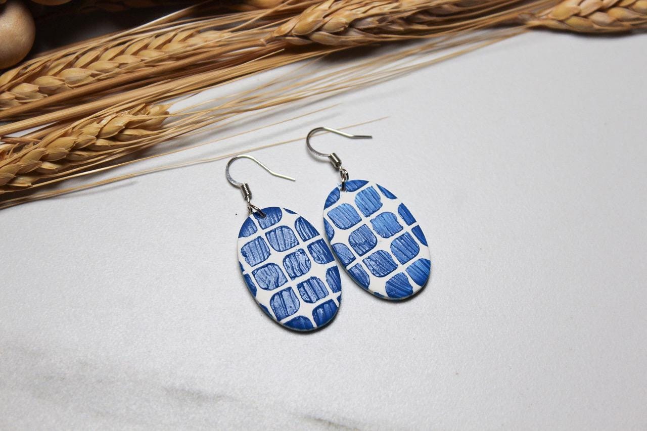 Blue patterned earrings on a light surface with dried wheat in the background