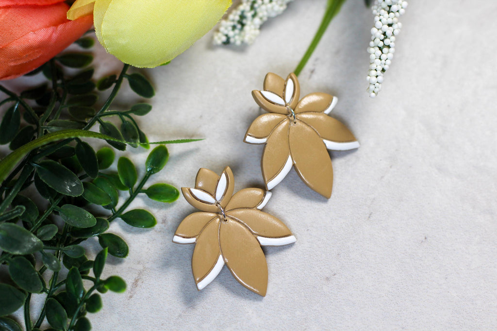 Latte brown floral earrings on a marble surface with greenery