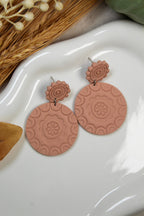 Pair of pink textured earrings on a white dish with decorative elements.