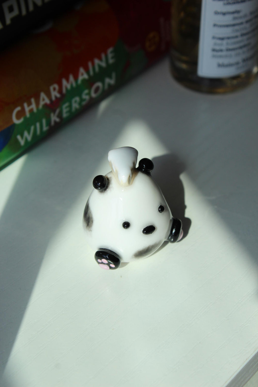 Small white figurine of a Panda with black accents and a piece of cake on a white surface, with a book titled 'Good Dirt' by Charmaine Wilkerson in the background.