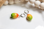 Pair of colorful mango-shaped earrings on a white surface with a blurred background.