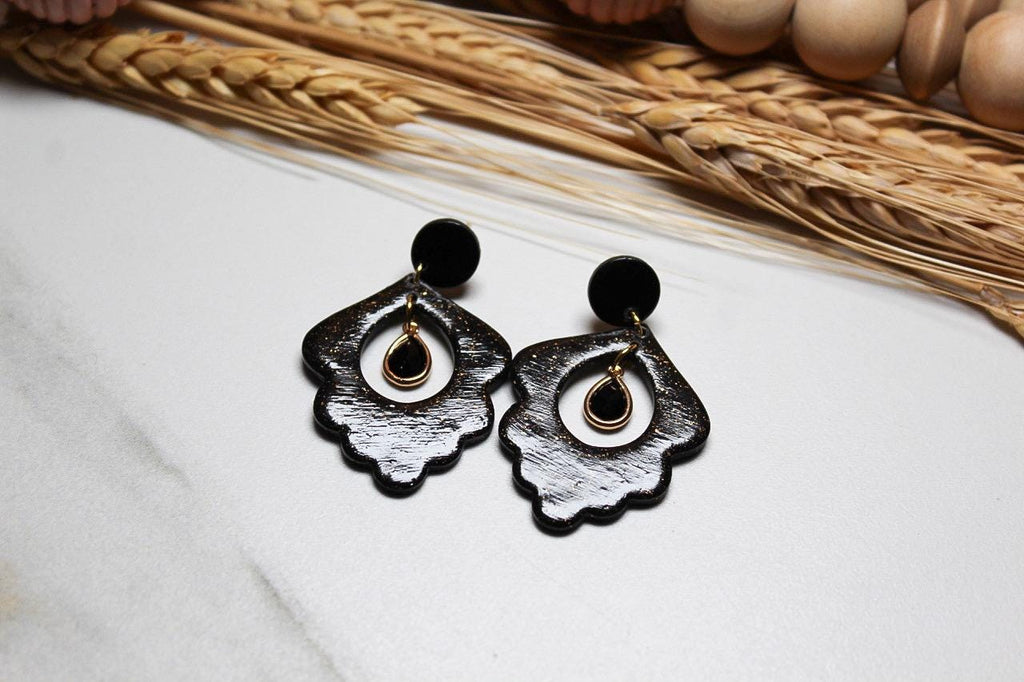 Black floral earrings on a white surface with dried plants in the background