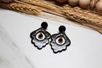Black floral earrings on a white surface with dried plants in the background