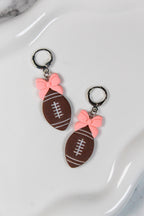 Football-shaped earrings with pink bows on a white surface