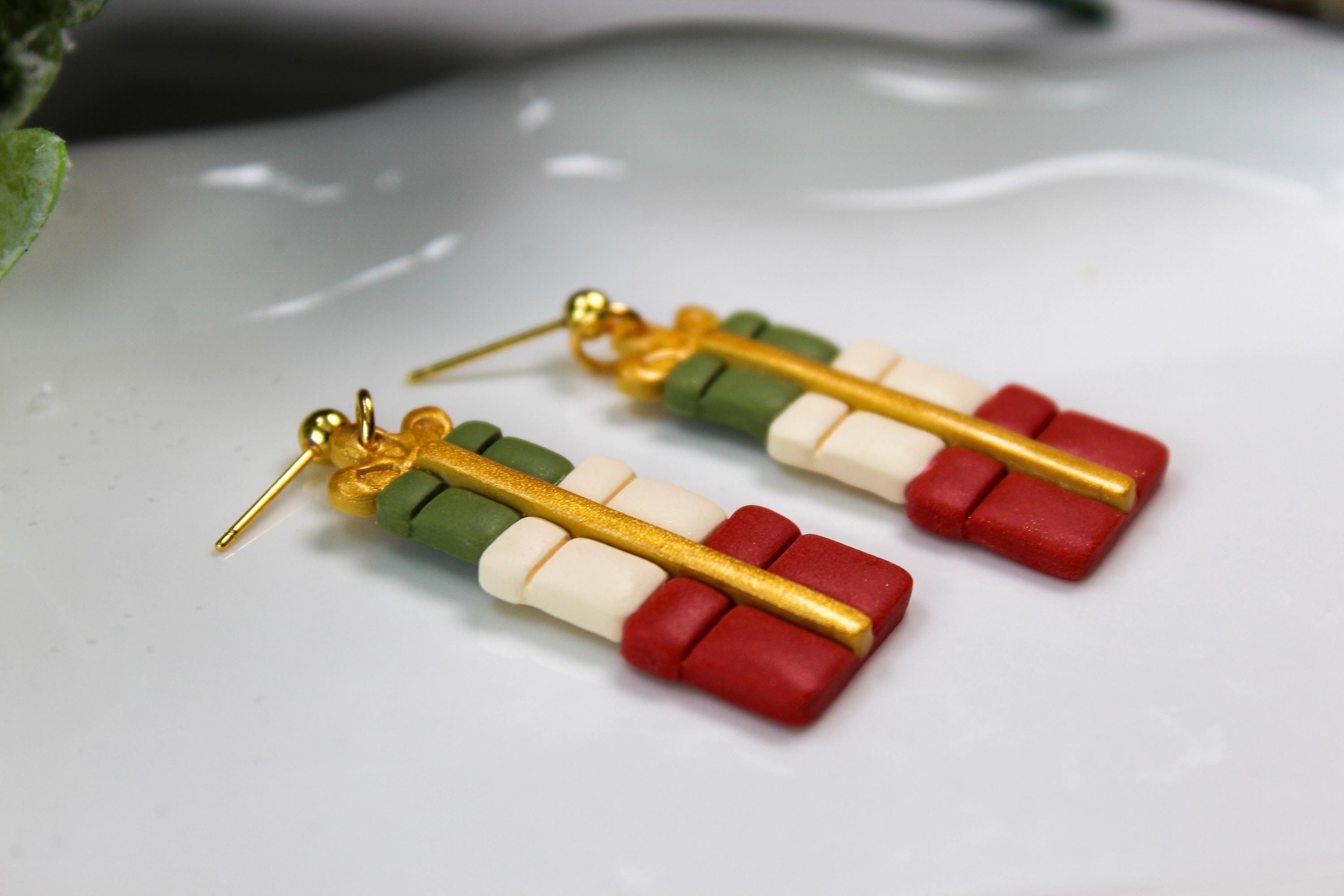 Christmas-themed gift box earrings on a white plate with greenery and pine cones.
