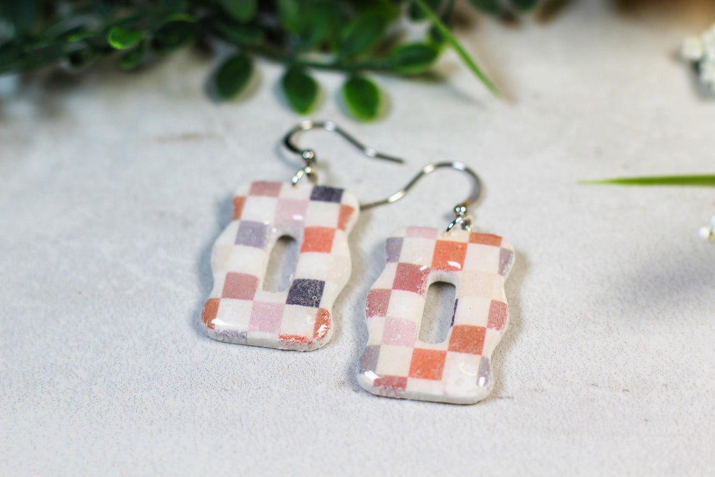 Pair of checkered earrings on a light surface with greenery in the background