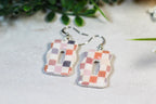 Pair of checkered earrings on a light surface with greenery in the background