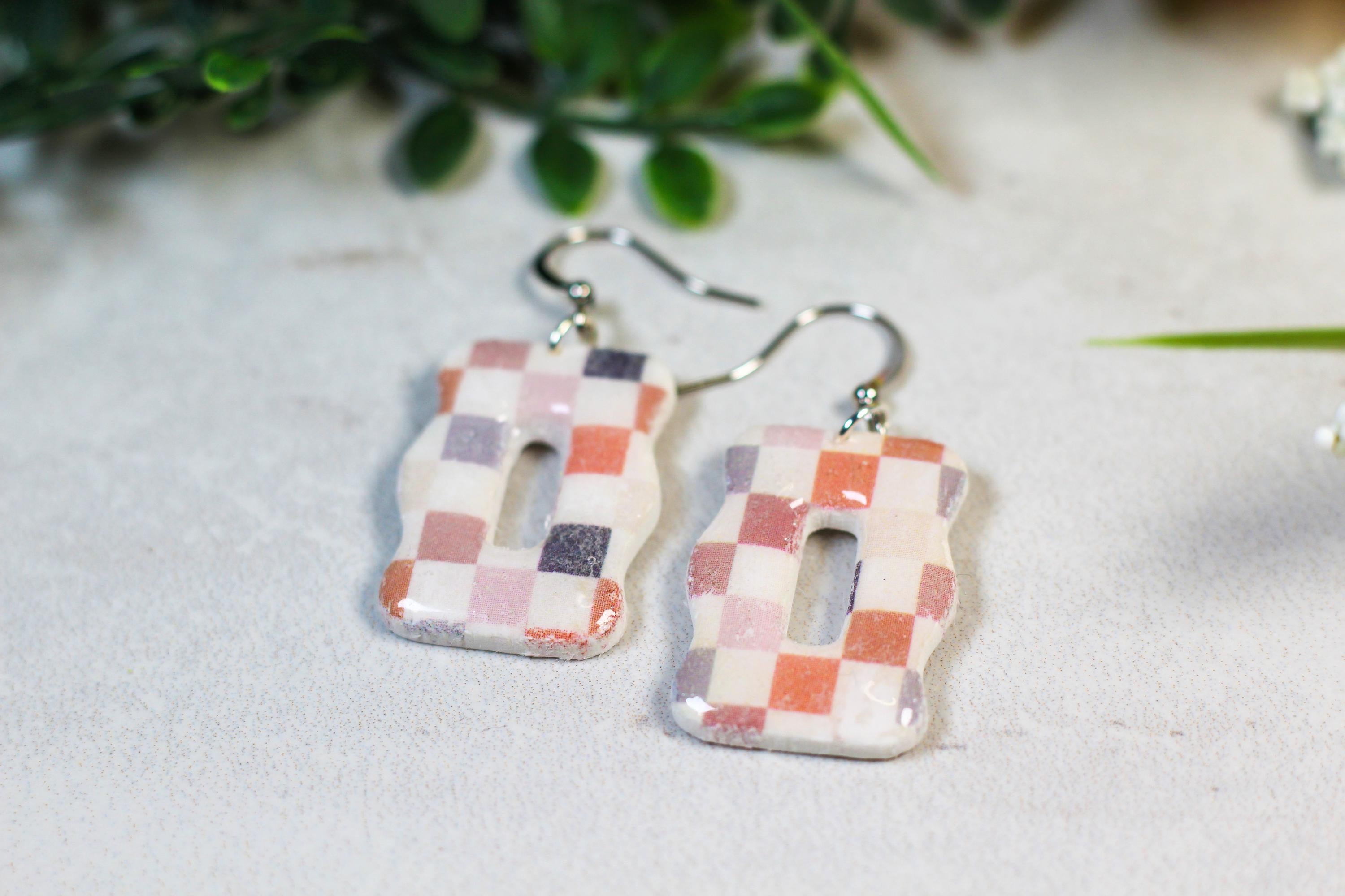 Pair of checkered earrings on a light surface with greenery in the background