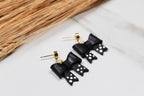 Black bow-shaped earrings with gold accents on a light surface.