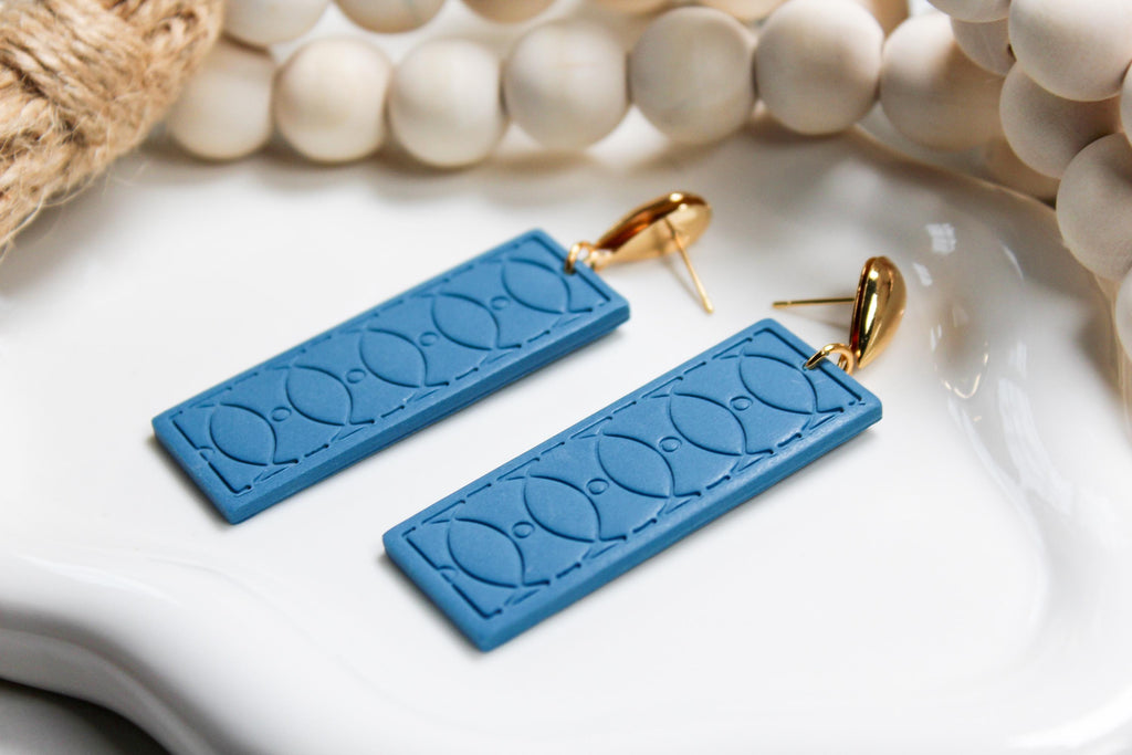 Blue textured earrings with gold hooks on a white surface with beads