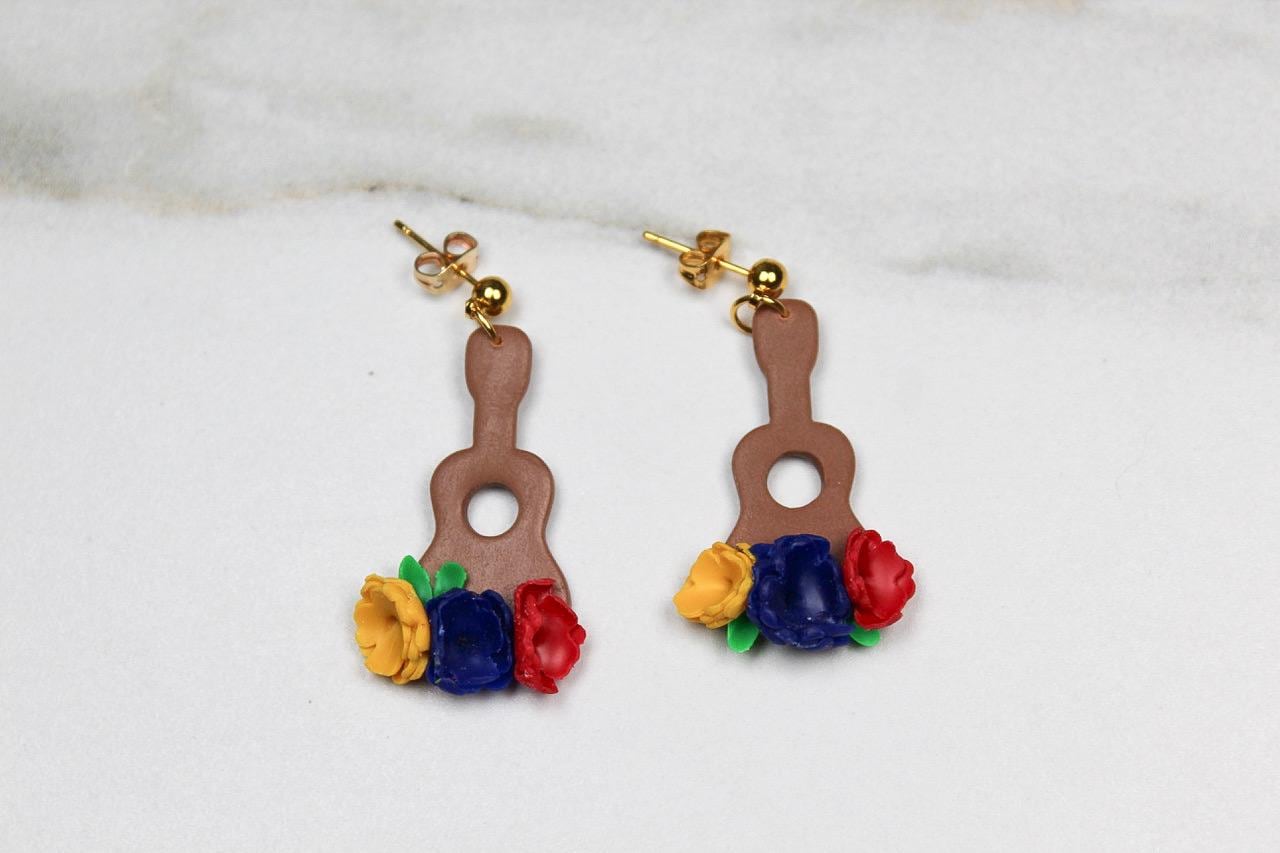 Pair of earrings shaped like guitars with floral tops on a light background